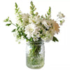 A bouquet of white flowers in a mason jar on a white background.