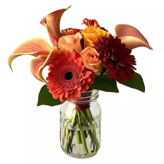 Bouquet of orange gerbera, roses, and lilies in a glass jar against a white background.