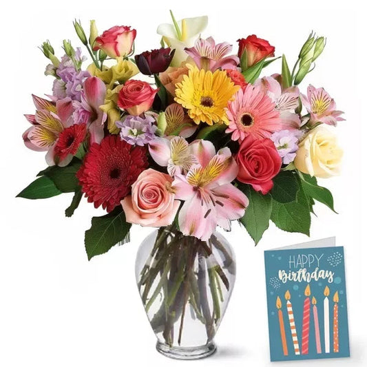 A colorful bouquet of mixed flowers in a clear vase with a 'Happy Birthday' card.