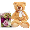 A plush teddy bear with a white bow tie next to a card with flowers.