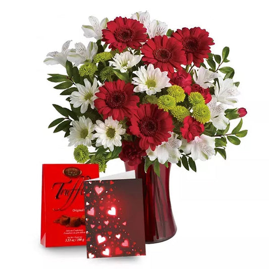 A bouquet of red and white flowers in a vase with a box of chocolates and a card with hearts.