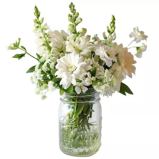 A bouquet of white flowers in a mason jar on a white background.
