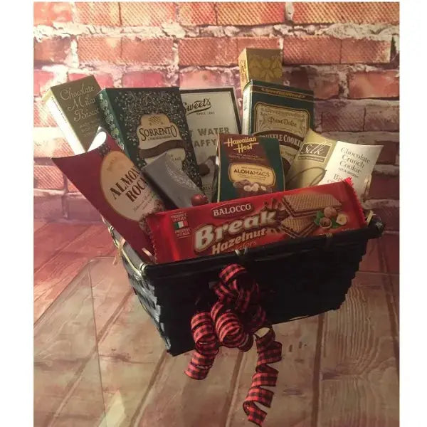Gift basket with assorted snacks and chocolates, decorated with a red bow, against a brick wall background.