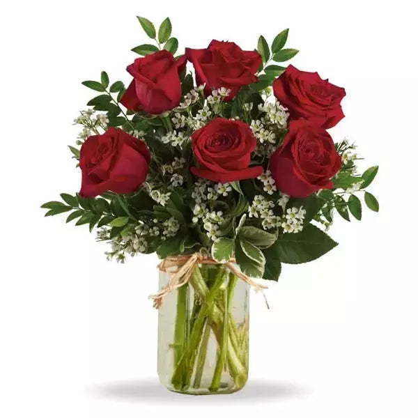 A bouquet of red roses and baby's breath in a glass jar with a raffia bow.